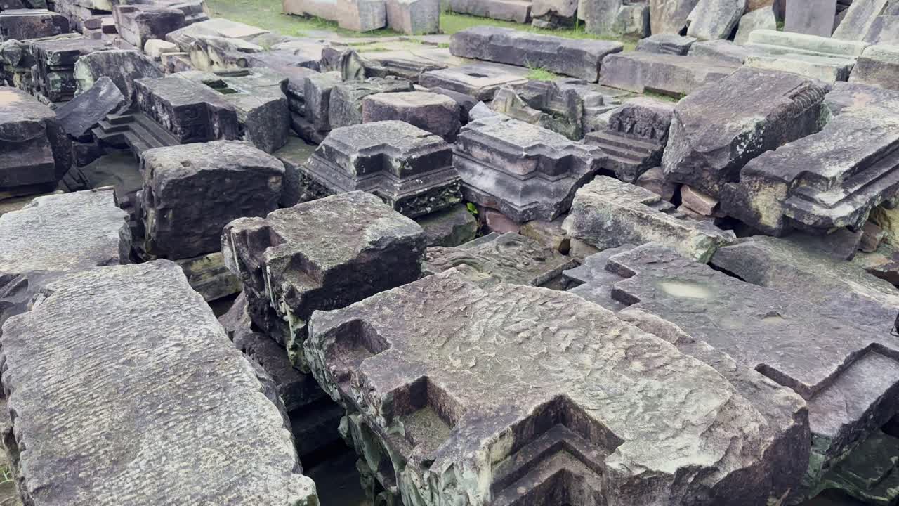The tilt-up shot begins on detailed stone blocks, slowly revealing a spread of ancient fragments—railings, pillars, and torana parts—remnants of the grand Sanchi Stupa complex