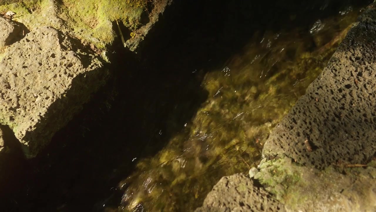 Água doce e límpida fluindo por um canal estreito de pedra sob a luz quente do sol.