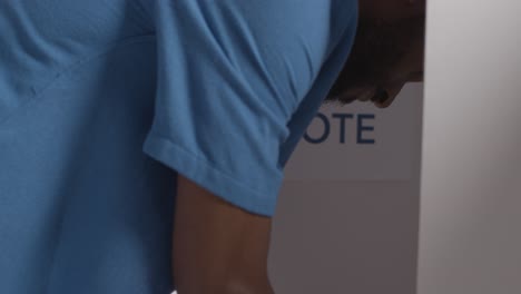 close up of man in booth with ballot paper in american election deciding how to cast his vote