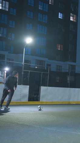 futbolista patea la pelota de fútbol hacia la meta durante una intensa sesión de entrenamiento nocturno en un campo urbano iluminado por las luces de la ciudad, rodeado de altos edificios residenciales y un vibrante cielo azul de la noche