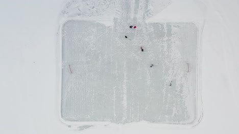 aerial top down, people playing ice hockey on small outdoor rink on frozen lake