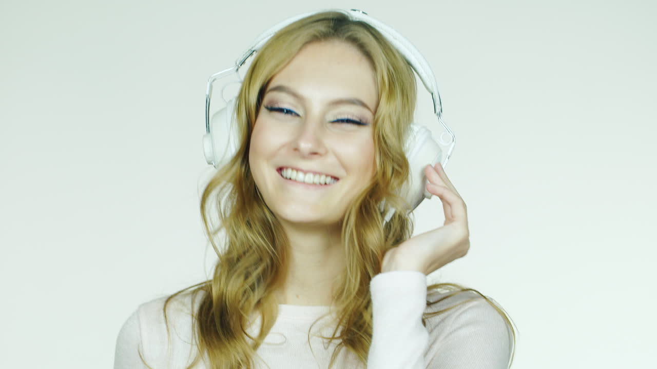 mujer atractiva bailando y escuchando un video musical filmado en el estudio con un fondo blanco