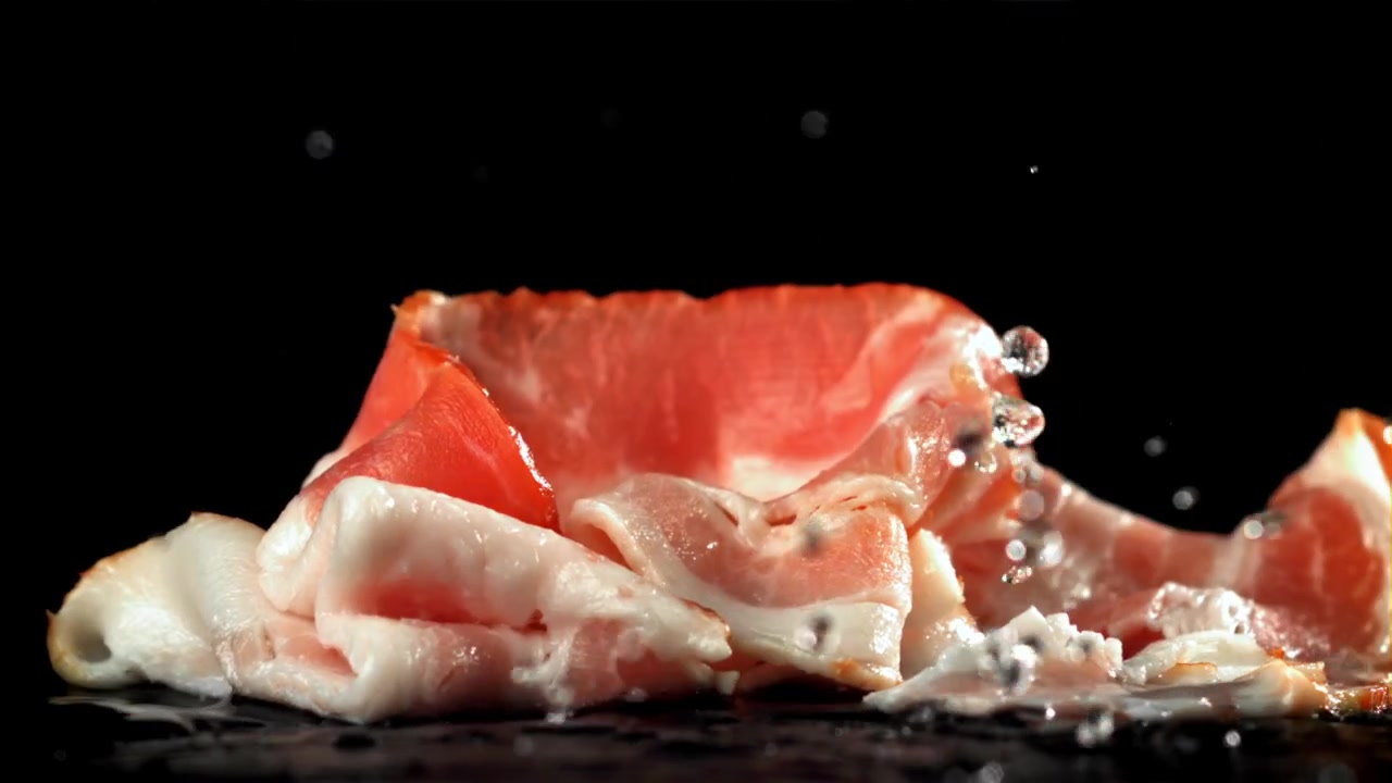 Fette di pancetta cruda che schizzano nell'acqua su sfondo nero al rallentatore