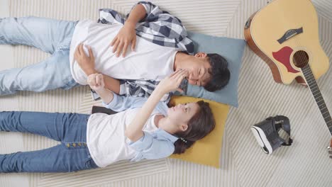 top view of asian teen couple recording voice message on smartphone while lying on carpet on the floor at home