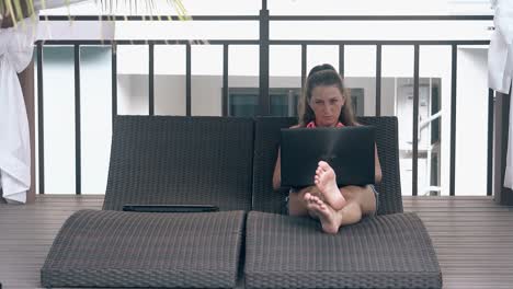 una mujer morena escribe en un portátil en un sofá acogedor en un hotel exótico