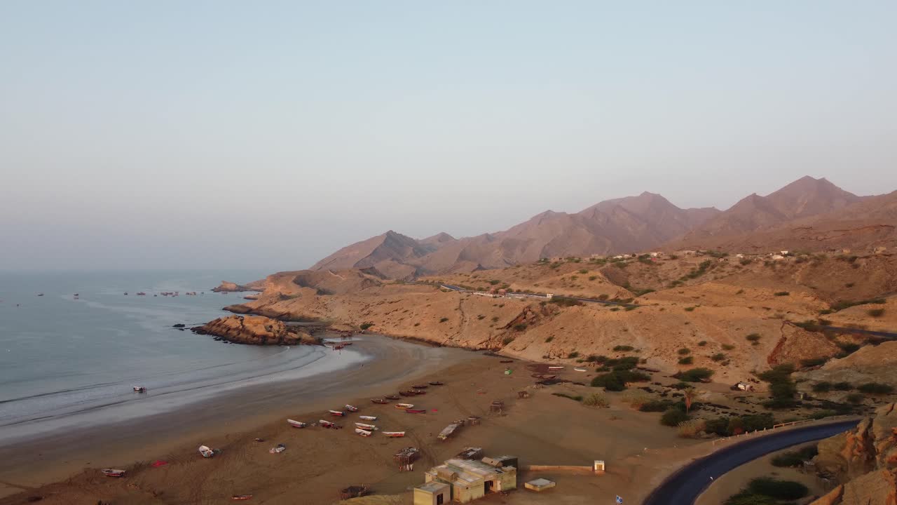 Inquadratura aerea con drone in tilt-up sopra la spiaggia di Kund Malir, lungo una strada accanto al parco nazionale di Ormara Hingol, con una catena montuosa sullo sfondo nel Balochistan.