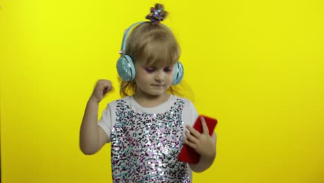 Child-dances-with-smartphone,-listening-to-music-on-headphones.-Little-kid-girl-dancing,-having-hun