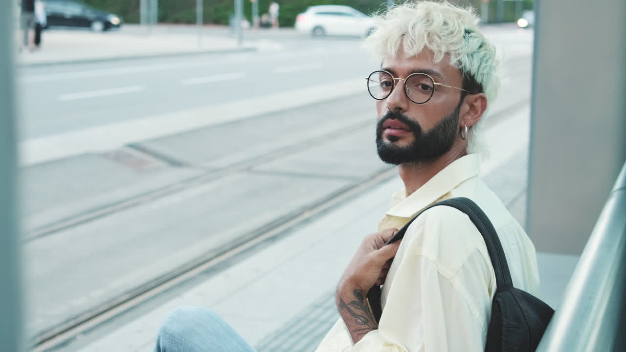 Giovane uomo con i capelli decolorati che aspetta a una fermata del tram in città