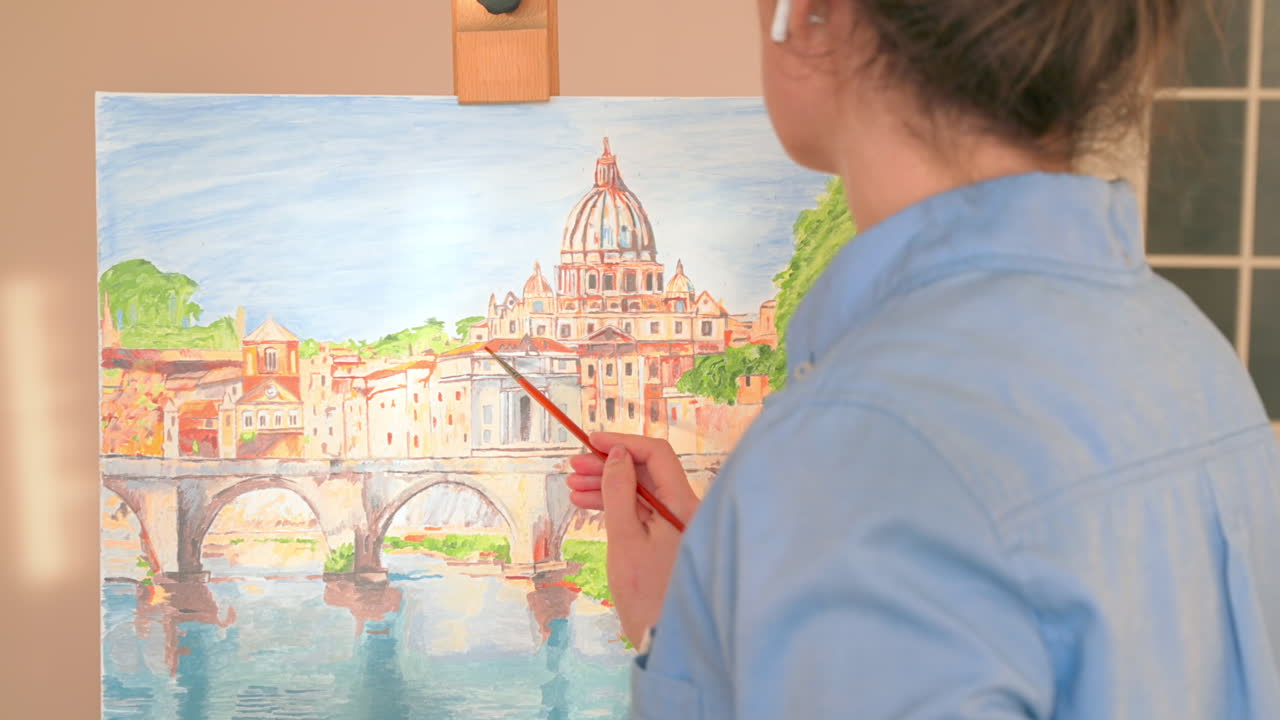 Caucasian woman painting a picture with a palette in her hands and listening music with earphones indoors