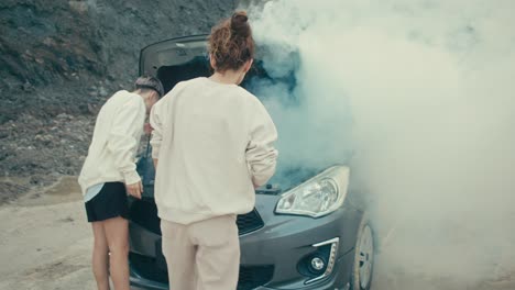 women trying to fix a broken-down car