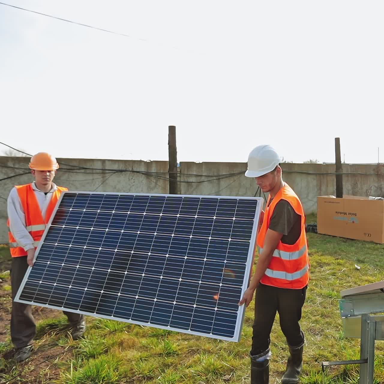 Installation of solar panels. Workers in protective uniform carrying blue solar battery in summer. Sustainable green energy.