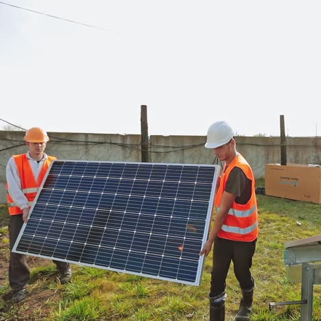 installation of solar panels. workers in protective uniform carrying blue solar battery in summer. sustainable green energy.