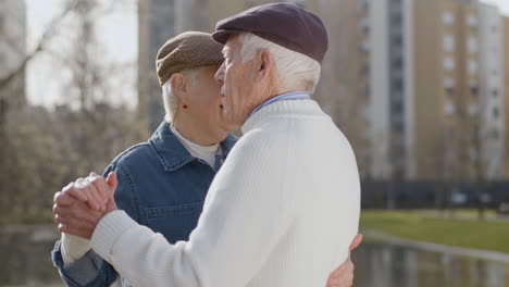 pareja de ancianos bailando en el parque de la ciudad en un cálido día de otoño con edificios de varios pisos en segundo plano