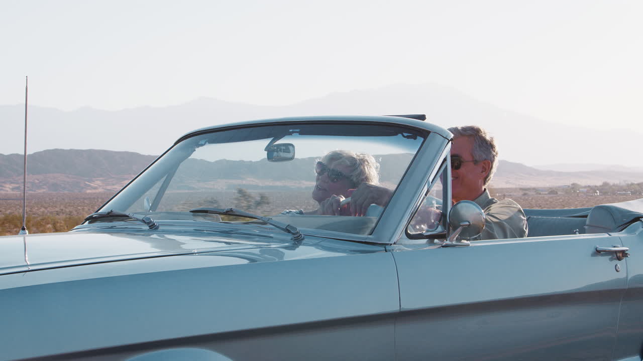 Lächelndes Seniorenpaar fährt Oldtimer-Cabrio auf der Autobahn