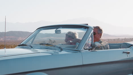 una pareja de mayores sonrientes conduciendo un descapotable clásico en la autopista.