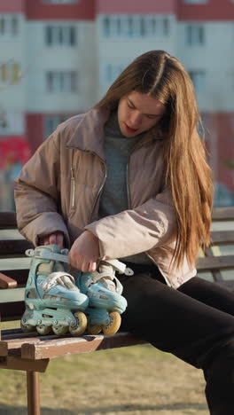 una chica con una chaqueta de melocotón, camisa interior gris y pantalones negros está sentada en un banco del parque con sus patines a su lado. momento tranquilo de descanso durante un día soleado en el parque