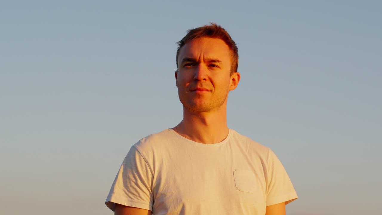 Young man standing against a sunset sky, looking contemplative and at peace