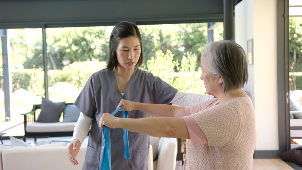 Helping senior asian woman with physical therapy, caregiver using resistance band at home