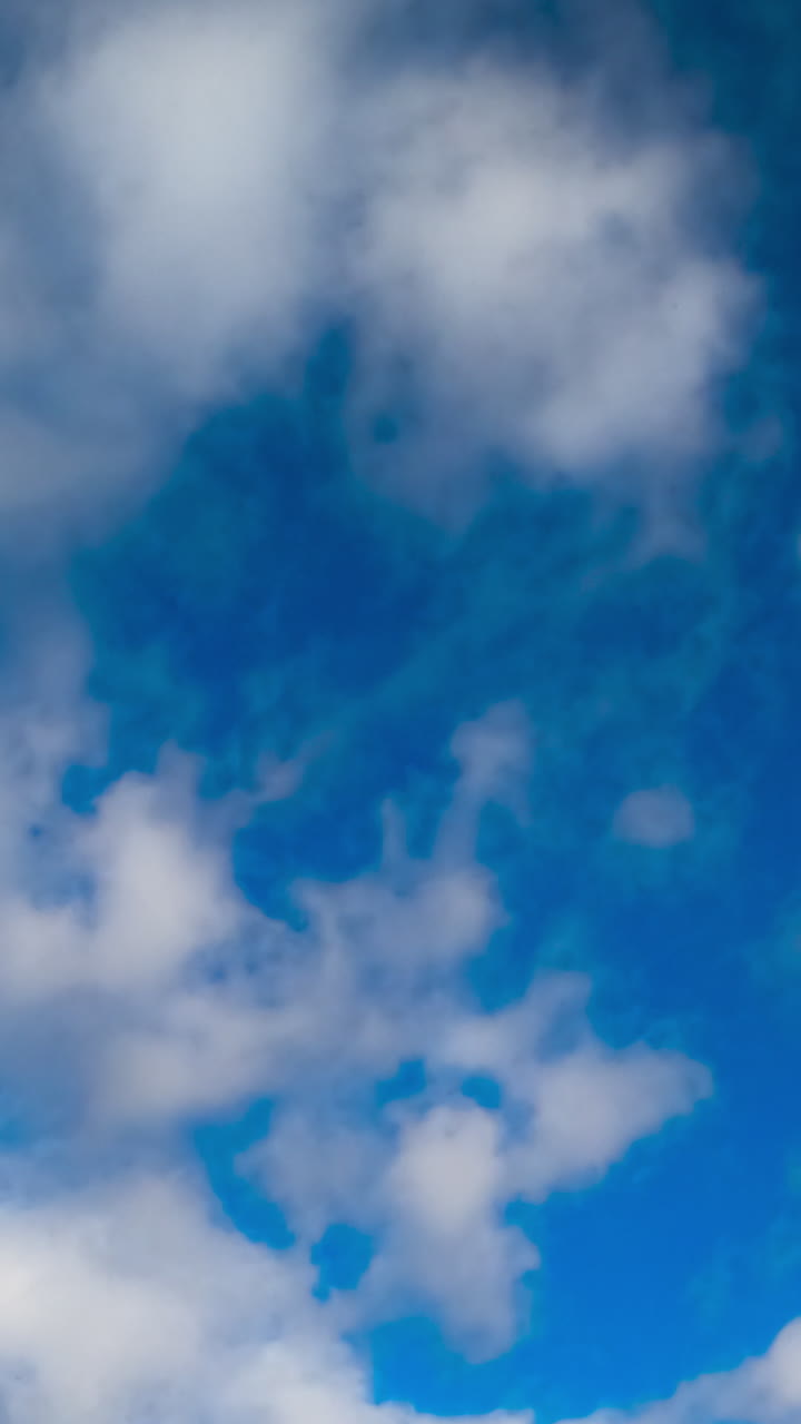 Blue summer sky with little soft white clouds floating quickly. Low angle view. Timelapse. Vertical video