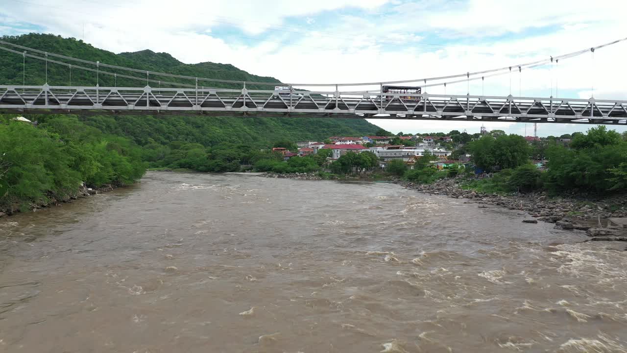 콜롬비아 혼다 타운 근처의 막달레나 강에서 다리 아래를 날고, 진흙 투성이의 물 위의 교통과 강둑의 녹색 풍경, 드론 샷
