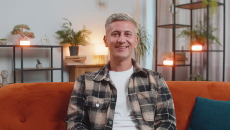 portrait of happy young caucasian man sitting on orange sofa looking at camera and smiling at home
