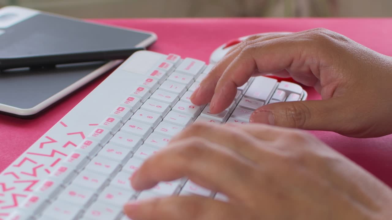 Woman's hand typing on a white keyboard with red letters, with graphic tablet in the background. On red table.