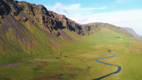 Areal-shot-of-beautiful-foothill-with-fresh-green-grass-and-narrow-river-somewhere-in-South-Iceland-during-summer.