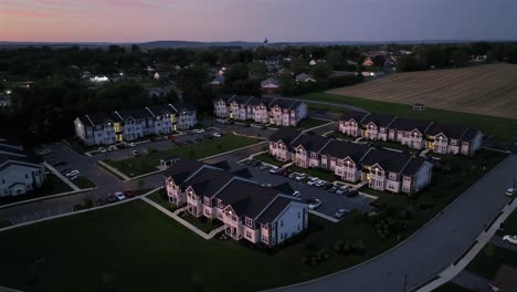 modern american townhouses with parking cars in small town of american at dusk. agricultural farm fields in suburb neighborhood in the evening. serene atmosphere ambiance in united states.aerial orbit
