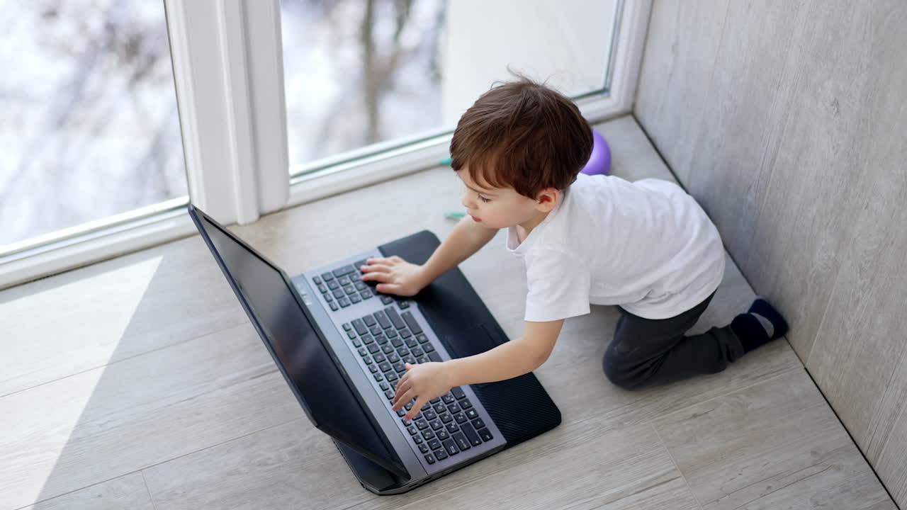 Lovely toddler presses the key on laptop and claps hands cheerfully. Kid points on screen and closes the device.
