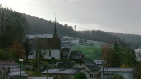 la nieve está cayendo lentamente por la iglesia y otras casas en el pueblo de cavergno.
