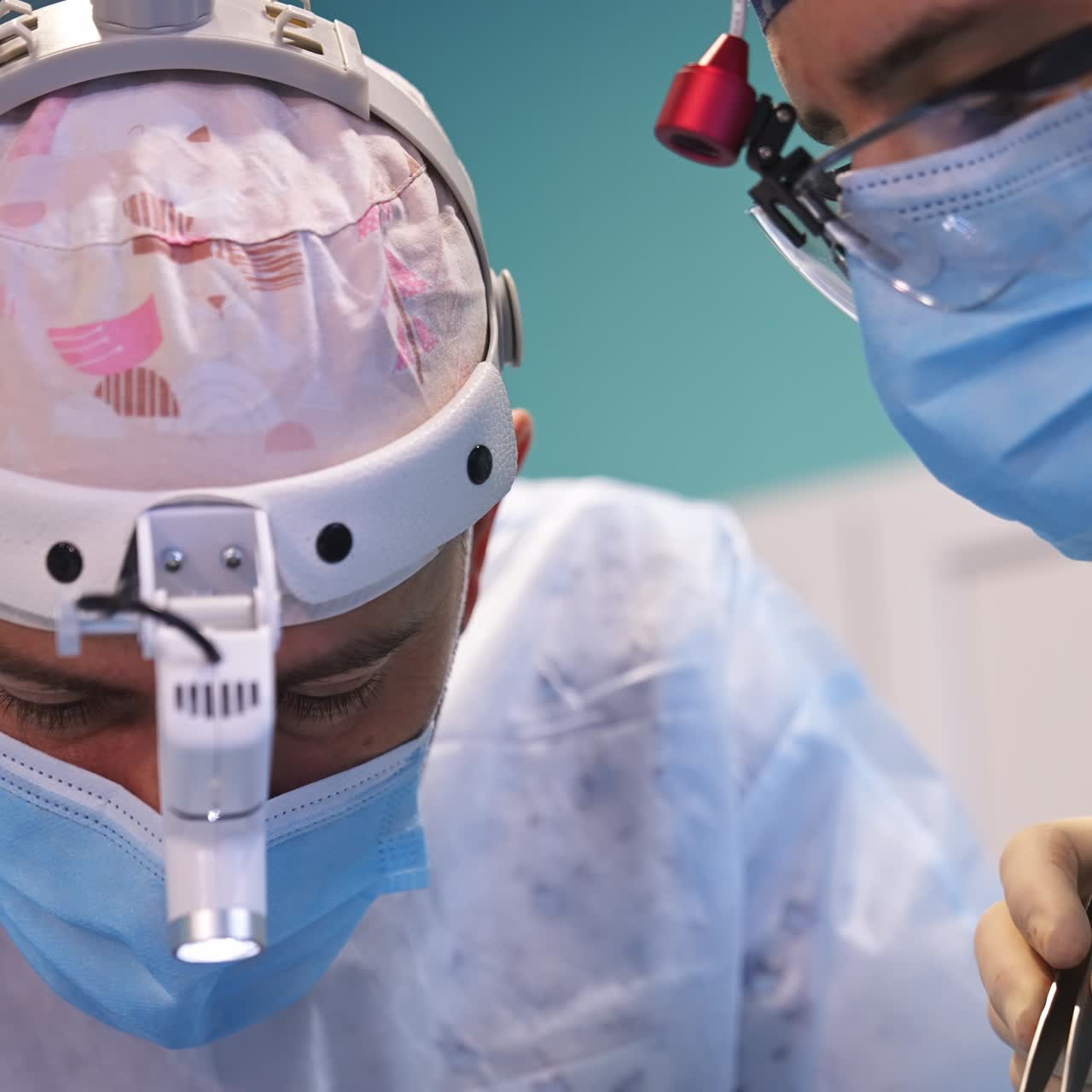 Mid-aged surgery professional in cap, mask and device glasses looks down at patient. Surgeons use tools at work. Close up