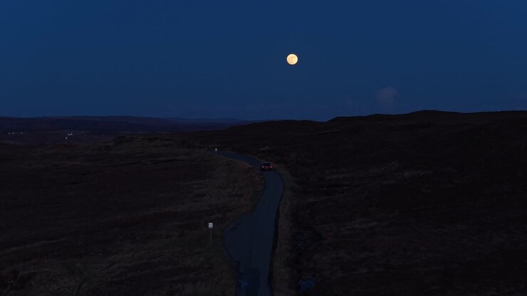 Auto in viaggio sotto la luna piena in Scozia.