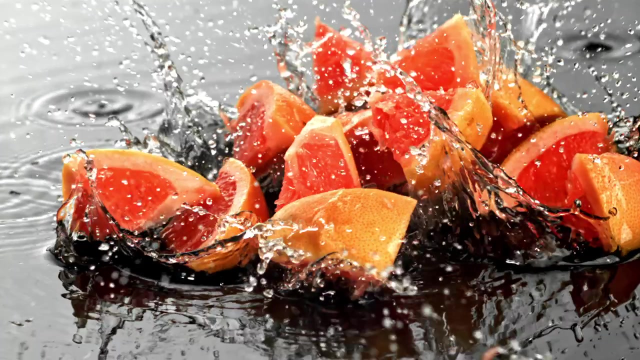 Friske grapefrugtskiver plasker i slowmotion ned i vand