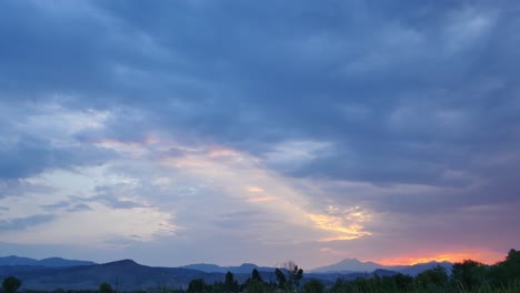 Extreme-wide-establishing-shot-of-blue-clouds-and-a-sunset-over-a-green-field-with-the-rocky-mountains-in-the-distance