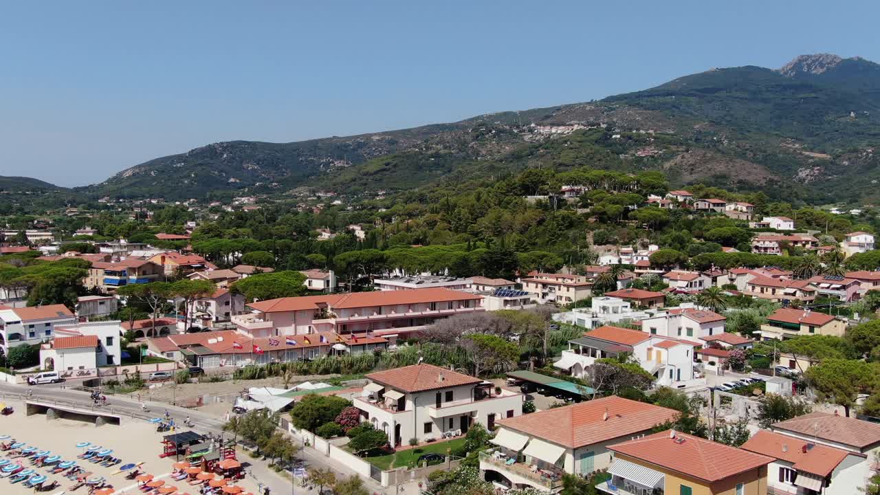 Boats bobbing in calm waters as people enjoy the sunny, vibrant shoreline of Isola d’Elba