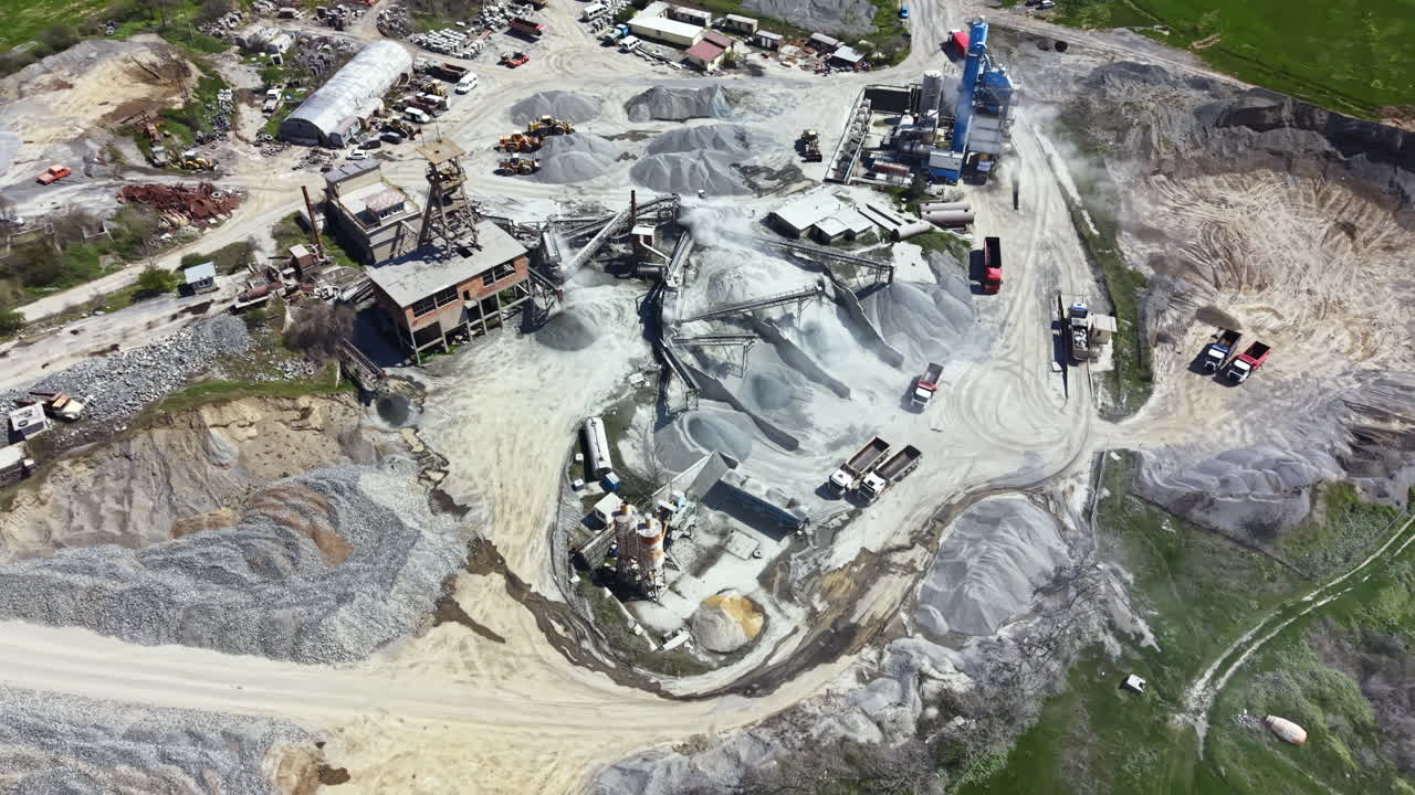 Granite quarry operation with machines, trucks, and processed stone in open area during daylight