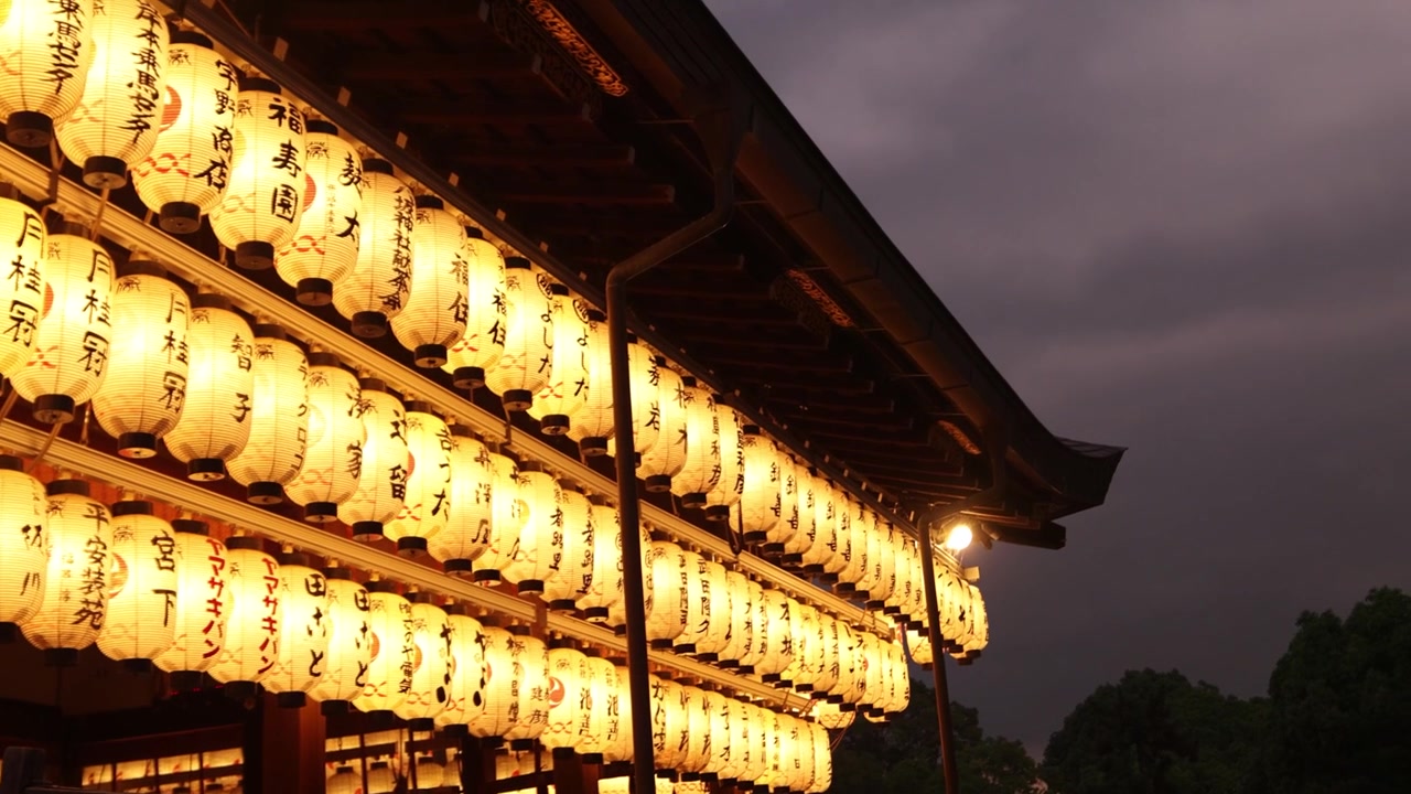 Rækker af oplyste lanterner pryder ydersiden af Yasaka-helligdommen om natten og kaster et varmt gyldent skær over det historiske Shinto-kompleks i Kyotos Gion-distrikt