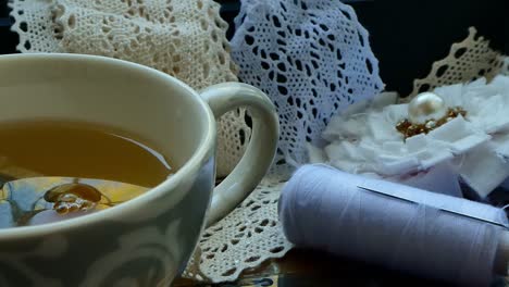 a hand of a woman leaving a coil of thread next to a cup of tea