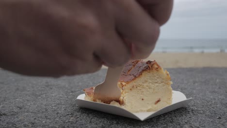 delicious slice of cheesecake with a wooden spoon, placed on a paper tray at the beach