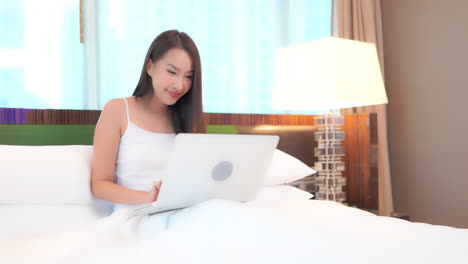 young woman celebrates good news while using laptop computer sitting in bed