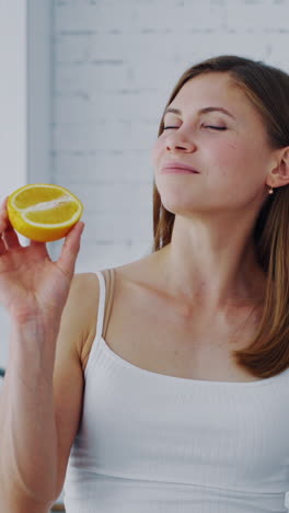 young woman with orange in cosy kitchen. healthy fruit in woman's hands indoors. beautiful female holding half of juicy orange. dieting concept. vertical video
