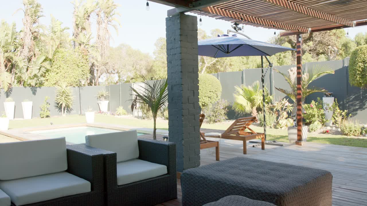 Camera is panning right and moving forward revealing patio seating ottoman pool umbrella backyard