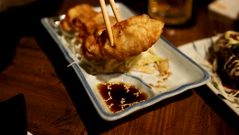 chopsticks lifting gyoza from a sauce dish