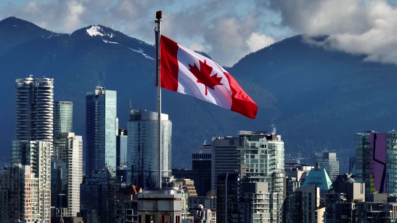 A View of the Canadian Flag Waving Against a Backdrop of Mountains and Modern High-rises, as Seen From South Granville in Downtown Vancouver, Canada - Zoom In Shot