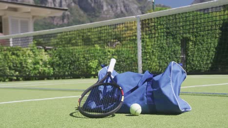 Bolsa-De-Deporte-Azul,-Raqueta-De-Tenis-Y-Pelota-En-La-Cancha-De-Tenis-En-Un-Día-Soleado