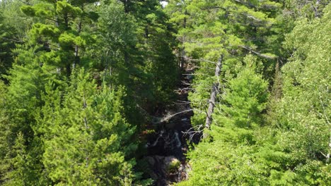 Aerial-landscape-view-of-a-peaceful-waterfall-flowing-through-a-green-forest-in-the-canadian-mountains,-Duchesnay-Falls,-Ontario