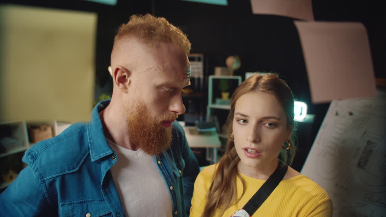 un chico y una chica hipsters cansados abrazándose cerca del tablero de pegatinas en una oficina oscura.