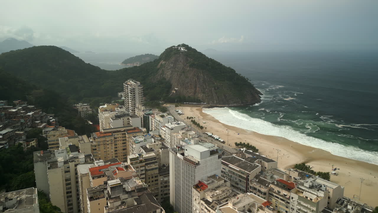 Stadsgebouwen van Copacabana en Pedra do Leme omringd door de oceaan op een bewolkte winterdag. Omhoog kantelende luchtglijvlucht opgenomen in 4K Apple ProRes 422.