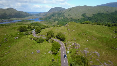 rising aerial video of tourists driving along winding roads on rugged scenery with lakes and mountains in background,location killarney national park