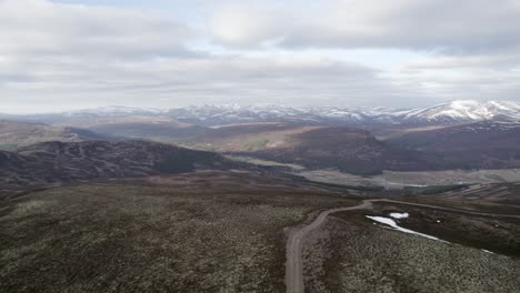 Filmische-Drohnenaufnahmen-Aus-Der-Luft,-Die-über-Wildes-Heidekraut,-Moorhuhn-Und-Flechtenheide-Fliegen,-Um-Eine-Berglandschaft-Mit-Schneeflecken-Und-Wolken-Zu-Enthüllen